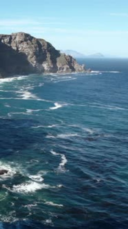 Sunlit Rocky Coast with Crashing Waves Remote Viewpoint Displaying Expansive Ocean and Rugged Cliffs