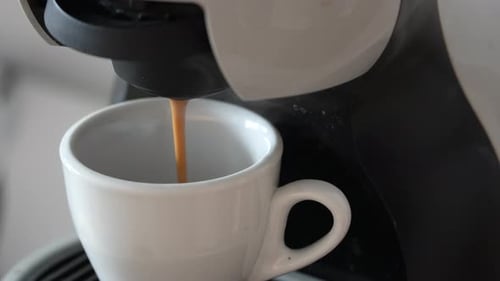A close-up shot of a coffee pouring fresh coffee into a white ceramic cup, capturing the rich, brown
