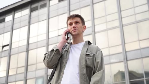 a young handsome man on the phone in front of a business center building