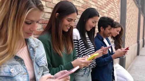 Young Group of Multiracial Friends Using Smartphone Leaning on Brick Wall