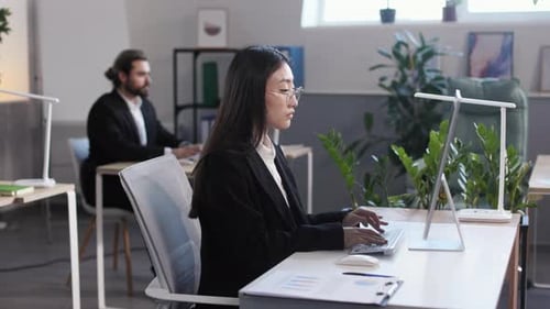 Asiatische Frau tippt im Büro auf der Tastatur des PCs