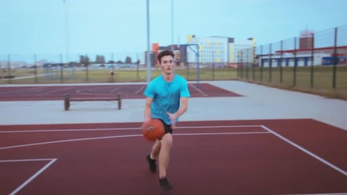 Teenager Boy Training with a Basketball at Sunset in Playground Throws the Ball Into the Basket Boy