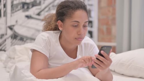 African American Woman using Smartphone while Lying on Stomach