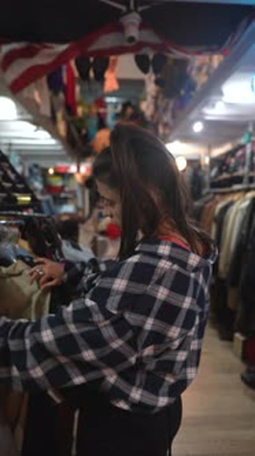 A Woman is Browsing in a Vintage Clothing Store Exploring Retro Styles and Colorful Outfits