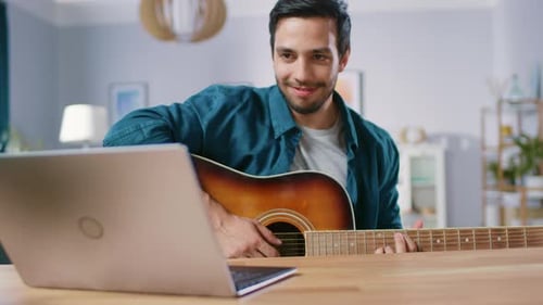 Man Plays Guitar at Home Using Laptop
