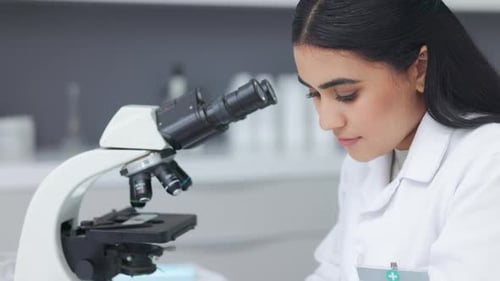 Young Adult Woman Looking Through Microscope in Laboratory