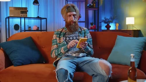 Portrait of Hippie Man Sitting on Sofa Using Smartphone Share Messages on Social Media Application