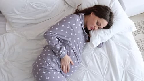 Pregnant Woman Resting in Bed, Hand on Baby Bump
