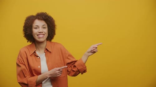 Woman Point at Copy Space and Looking at Camera on Yellow