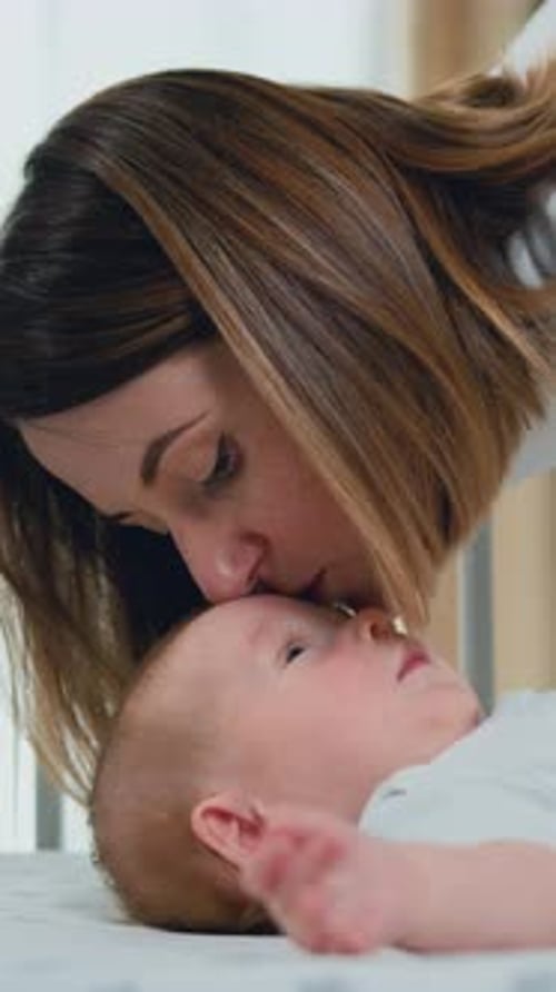 Close Up of Young Mother Hugging and Kissing Her Adorable Few Month Baby Resting in Crib and Smiling