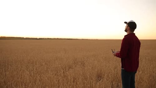 Farmer Holds Remote Controller with His Hands While Quadcopter is Flying on Background Drone Ascends