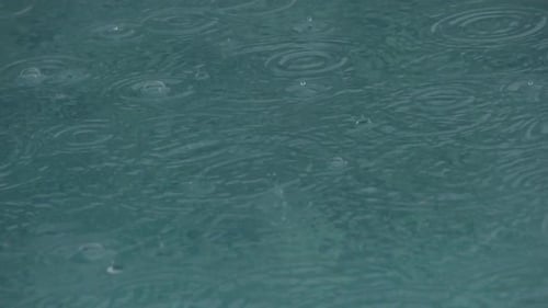 Super slow motion shot of raindrops falling on a quite water surface creating rings