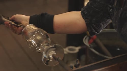 A woman using an instrument to mold a piece of glass