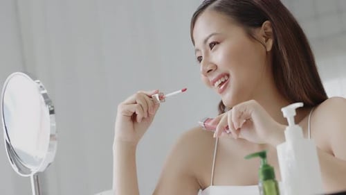 Close up shot young Asian beautiful woman looking mirror among cosmetic and painting lipstick.