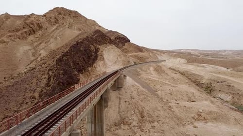 aerial slow slide drone shot of an empty train rail bridge, revealing a mountain and the desert in d