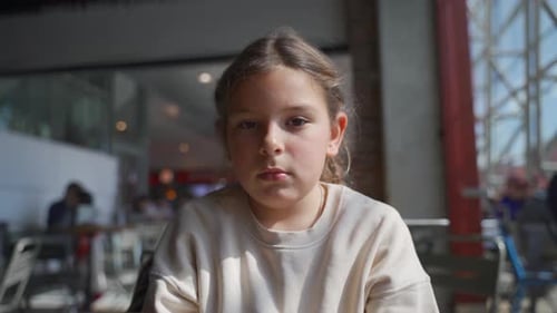Child in Thoughtful Transition From Focused to Relaxed Mood in a Busy Cafe Setting