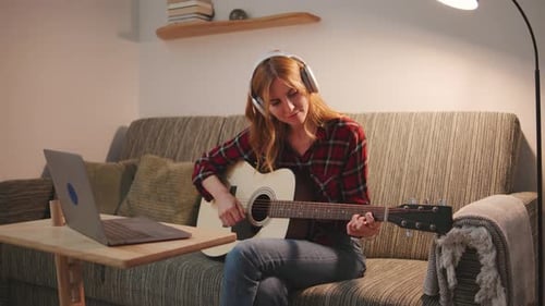 Woman with Headphones Plays Acoustic Guitar on Couch
