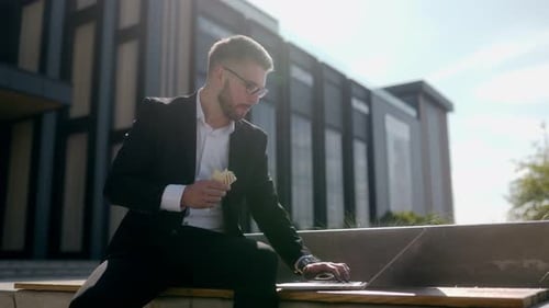 Entrepreneur Multitasking Sandwich in Hand Typing on Laptop in City Center