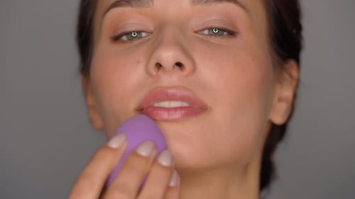 Woman Applying Makeup with Purple Sponge, Close Up