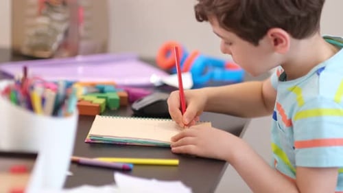 Boy Drawing with Red Pencil at Desk