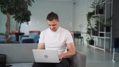 young handsome man works on a laptop in the office and then finishes his work with relief
