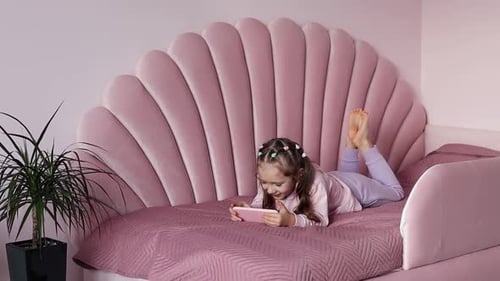 Smiling Child Lies in Bed Using Smartphone