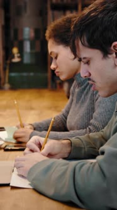 Two young adults writing together indoors at a table