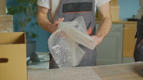 Hands Workers of Moving Company With Uniforms Carefully Packing Dishes at Boxes