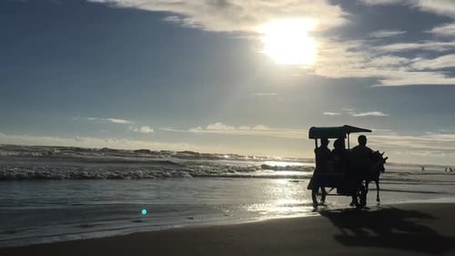 Wunderschöner Sonnenuntergang mit vorbeifahrendem Pferdewagen am schwarzen Sandstrand von Parangtritis