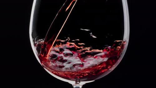 Red wine is pouring into a glass on a black background. Close shot.