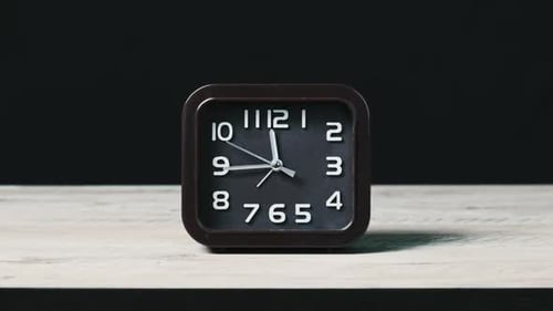 Reloj analógico sobre mesa de madera y fondo negro que muestra la hora