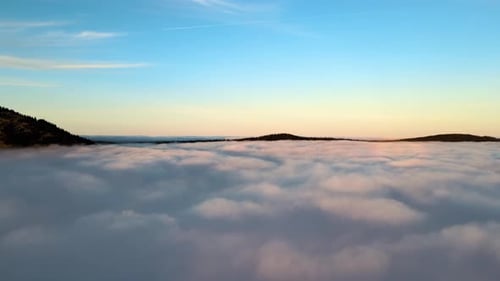 Aerial View of Yellow Sunset Over White Puffy Clouds with Distant Mountains on Horizon