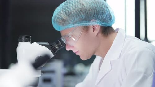 Focused Young Man Using Microscope in Modern Laboratory