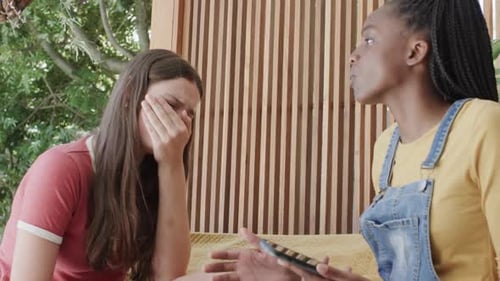 Sad diverse teenage female friends talking and covering face in slow motion
