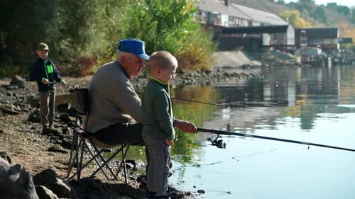A grandfather and his grandchildren are fishing on the river bank.