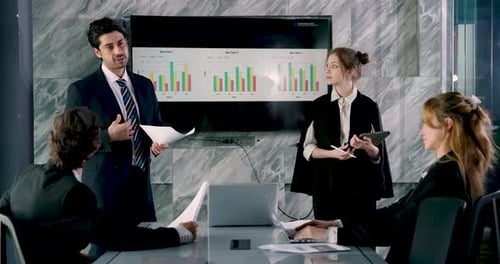 Confident businessman explaining report during office meeting while team members read documents,