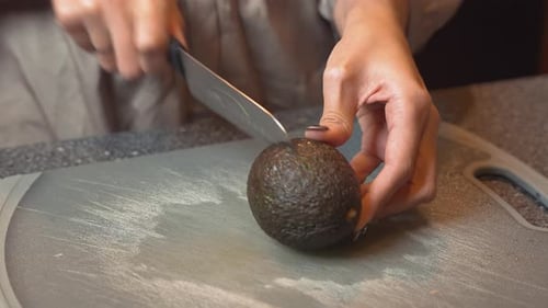 Woman cuts an avocado in half with knife