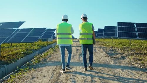 Shot Back Two Men on the Solar Farm in Special Uniform Walking Discuss the Installation of Sunny