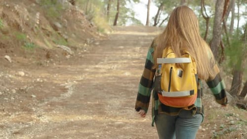 Following a Young Woman with a Bright Backpack as She Ascends a High Mountain, Walking along.