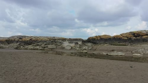 Tracking shot of along the flat sand showing some small rock cliffs on the uk coast line.