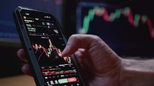 Trader Man Hand Holding Smartphone Using Trading Application with Stock Market Charts Bitcoin or USD