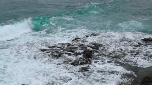Waves crashing into a rocky formation near the shoreline of a large wave breaking over stones on the