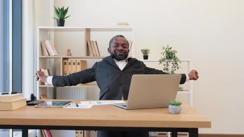 Exhausted Man Sitting at Office Desk with Portable Laptop