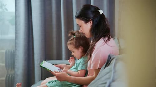 Woman Reads Book with Child on Couch Indoors