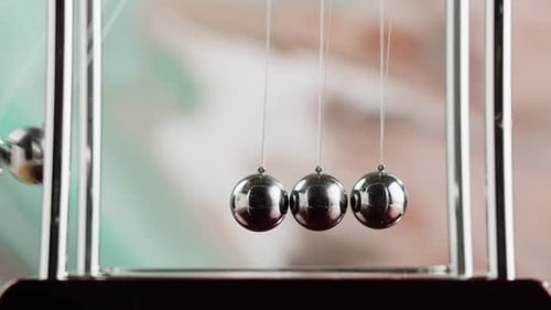Hand starts Newton's Cradle with swinging metal balls