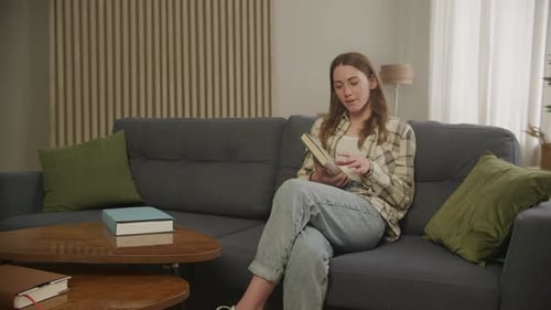 Woman Reads Book on Couch Indoors During Daytime