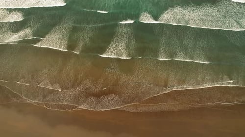 Overhead view of ocean waves washing onto sandy shallow tropical shoreline
