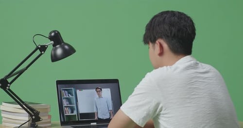 Asian Male Looking At A Male Teacher Teaching On A Laptop While Studying On Green Screen