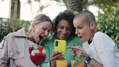 Three Women Looking at Phone and Laughing Outdoors