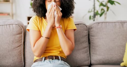 Woman Blowing Nose with Tissue While Sitting on Couch